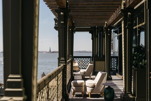 A balcony with outdoor seating, a view of the water, and a distant cityscape.