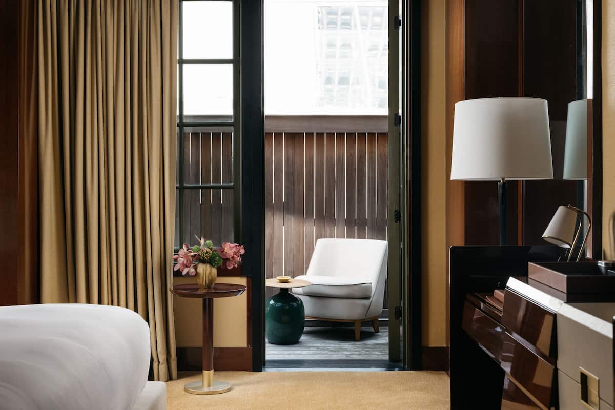 Une chambre d’hôtel avec un lit, un bureau, une chaise, une lampe et une vue sur l’extérieur.