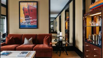 Eine Hotellobby mit einem roten Sofa, einem Couchtisch, einem Poster, einem runden Tisch mit Lampen und einer Kommode mit Flaschen.
