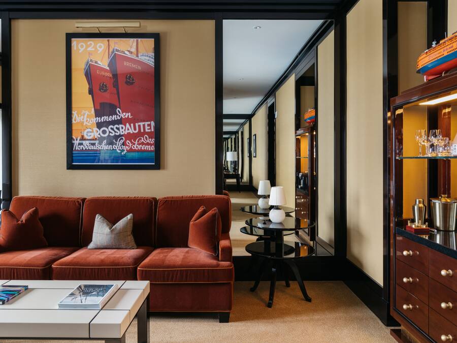 Eine Hotellobby mit einem roten Sofa, einem Couchtisch, einem Poster, einem runden Tisch mit Lampen und einer Kommode mit Flaschen.