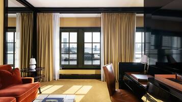 Habitación de hotel con vista a la ciudad, un sofá rojo, un sillón de cuero marrón, un escritorio y un piano.