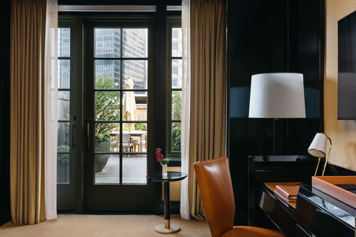 Une chambre d’hôtel avec une grande fenêtre, un bureau avec une lampe et une chaise.