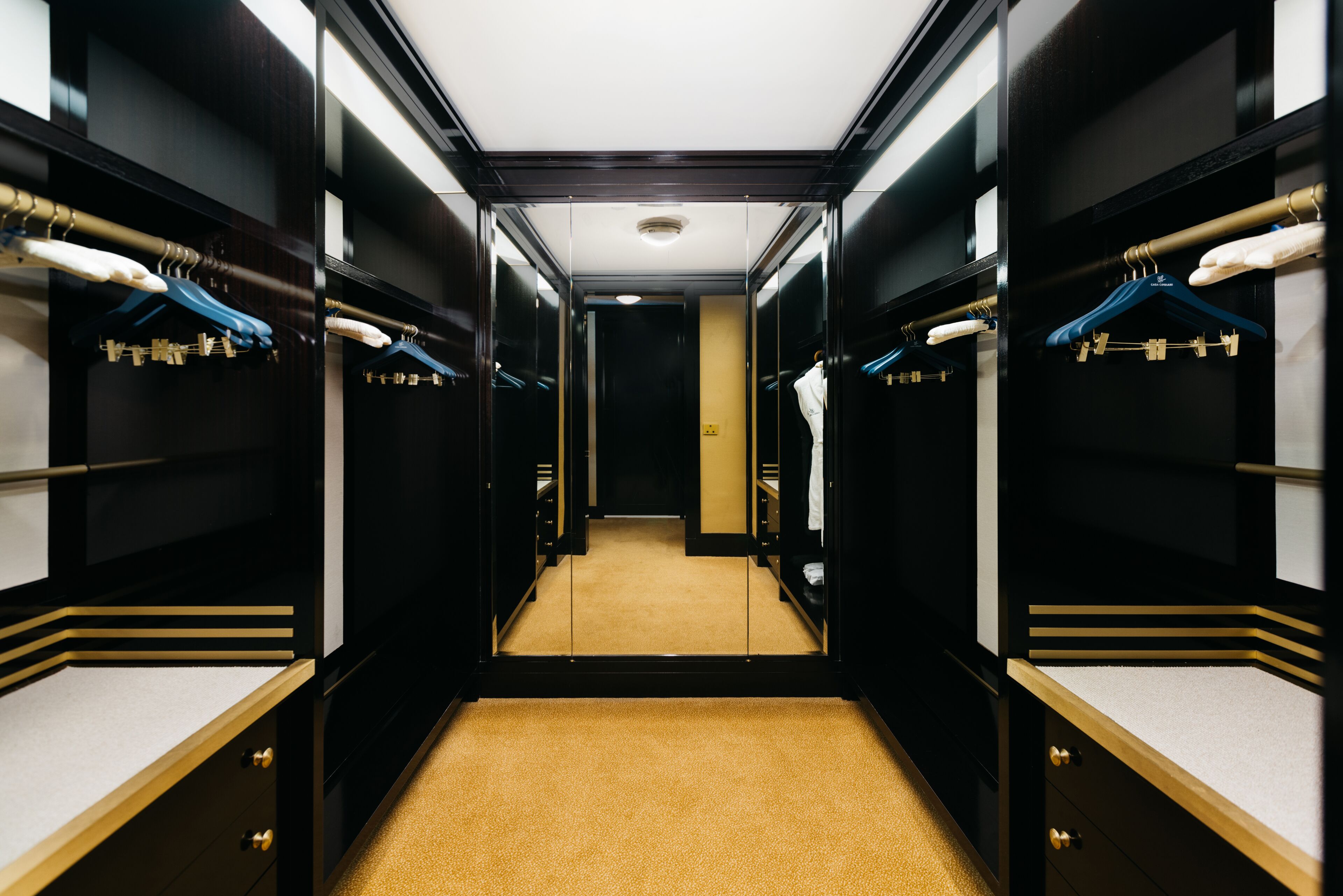 A hotel corridor with mirrored closet doors, a carpeted floor, and a central light fixture.