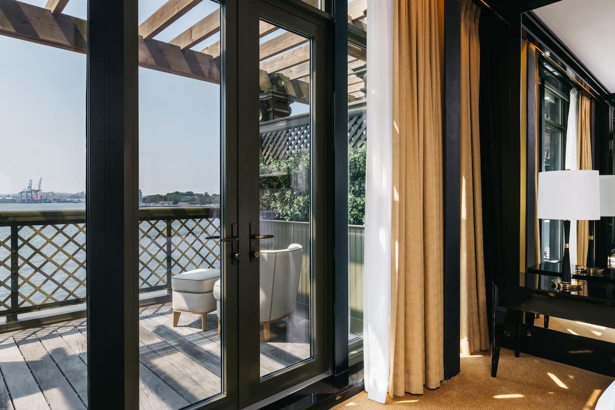 Un balcon doté d’une terrasse en bois, d’une chaise blanche et d’une table avec une lampe.
