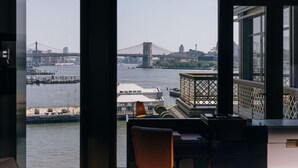 Uitzicht vanuit een kamer met grote ramen op een rivier, een brug en een waterkant met gebouwen en een steiger.