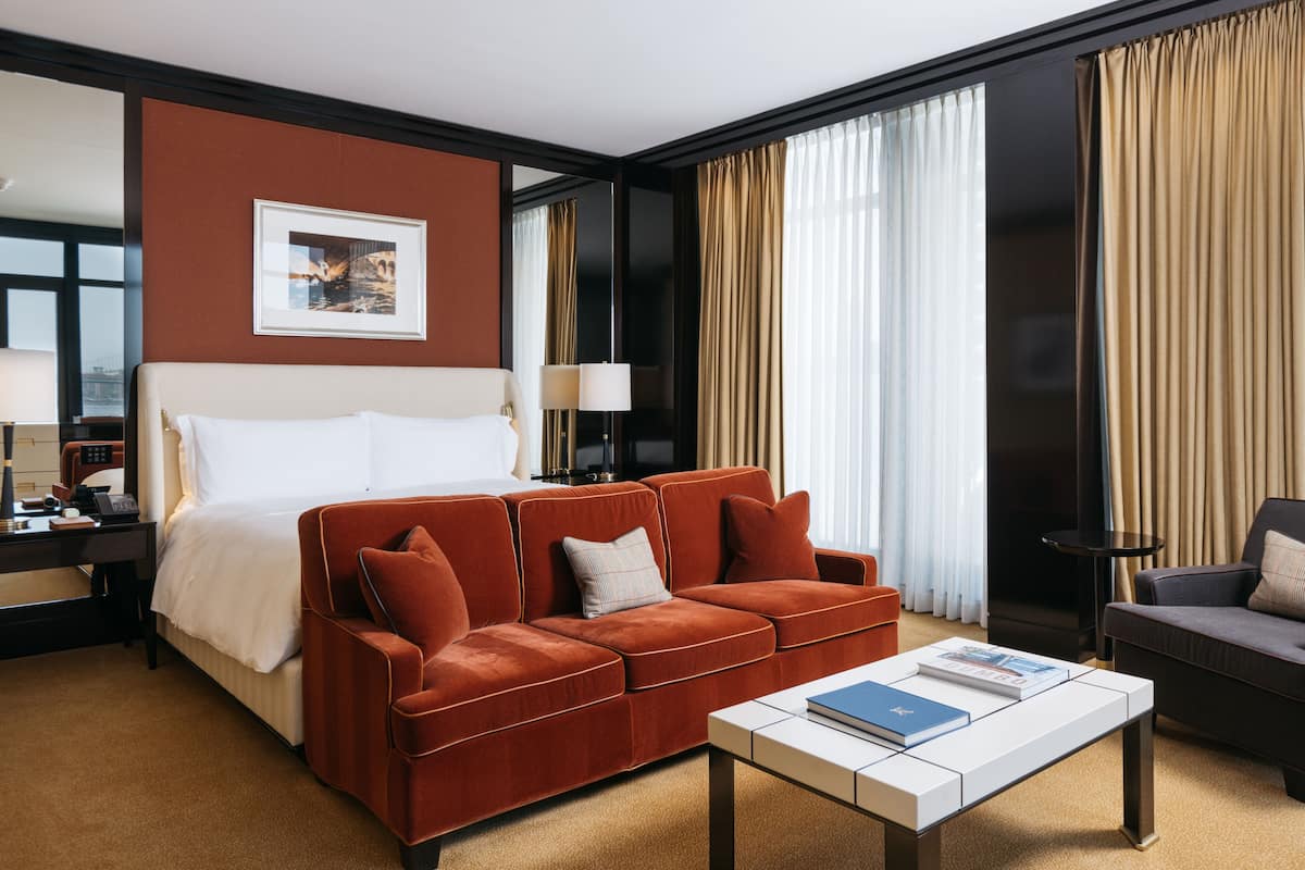 Une chambre d’hôtel avec un grand lit, un canapé rouge, une table basse blanche et un téléviseur.