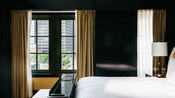 Ein Hotelzimmer mit Bett, Schreibtisch, Lampe und einem fenster mit Vorhängen.