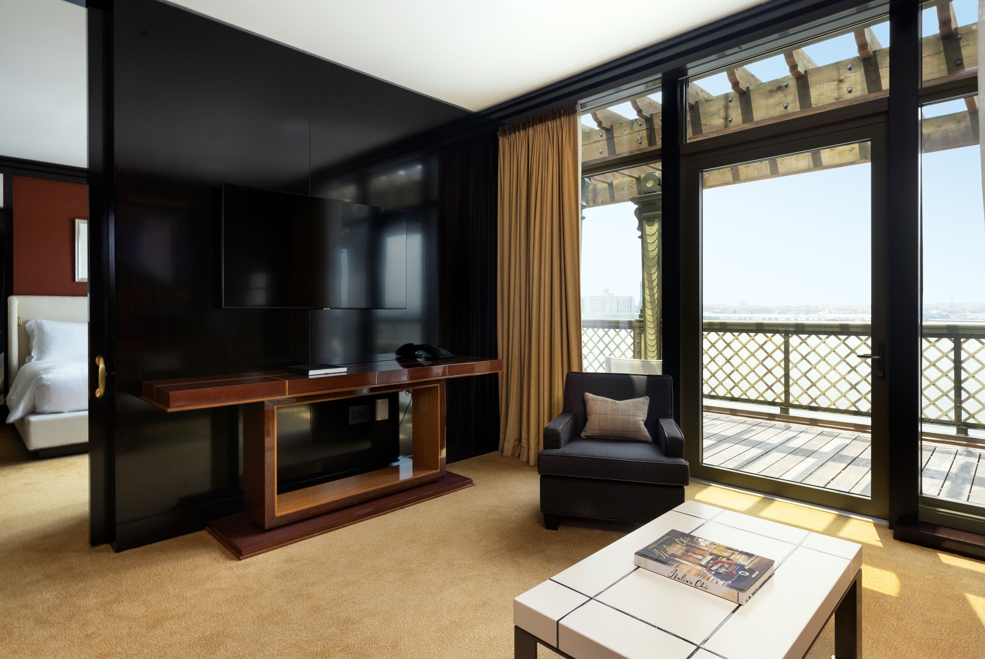 Habitación de hotel moderna con una televisión de pantalla plana grande, un sofá, una mesa de centro y un balcón con vista a la ciudad.