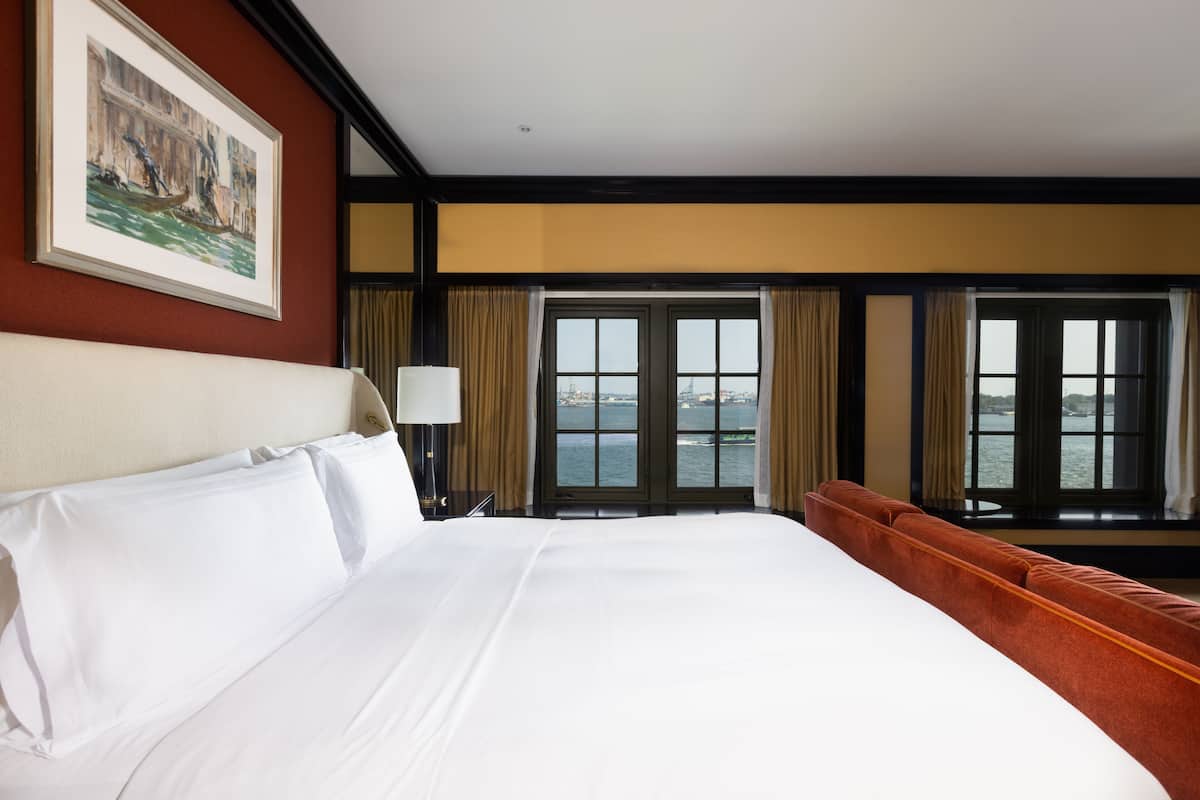 Une chambre d’hôtel avec un grand lit, une vue sur l’eau par les fenêtres et un tableau encadré au mur.
