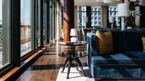 Een moderne hotellobby met een groot raam, een blauwe bank, een ronde tafel en meerdere lampen.