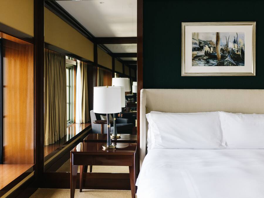 Una camera d'albergo con un letto grande, un comodino, una lampada, un quadro incorniciato e vista sul corridoio.