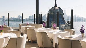 Een dakrestaurant met gedekte tafels, met uitzicht op een stadszicht en een wateroppervlak.