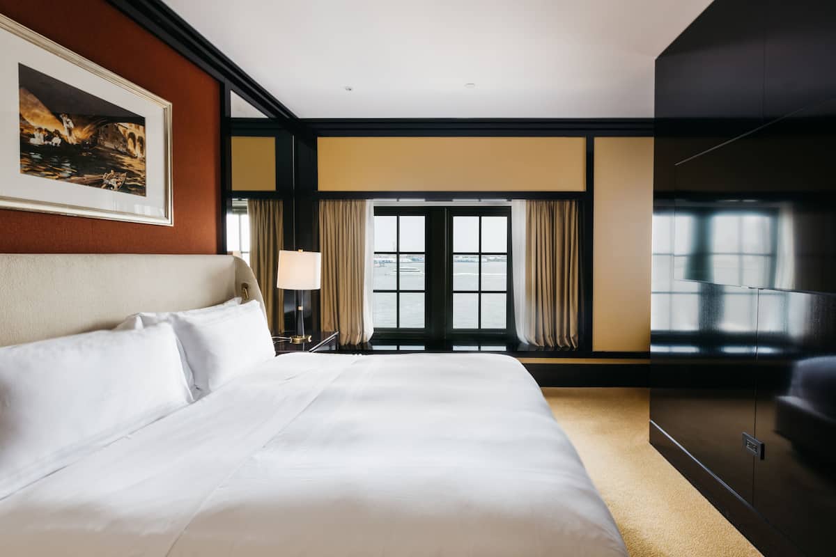 Une chambre d’hôtel avec un grand lit, une télévision, un tableau au mur et une fenêtre avec des rideaux.
