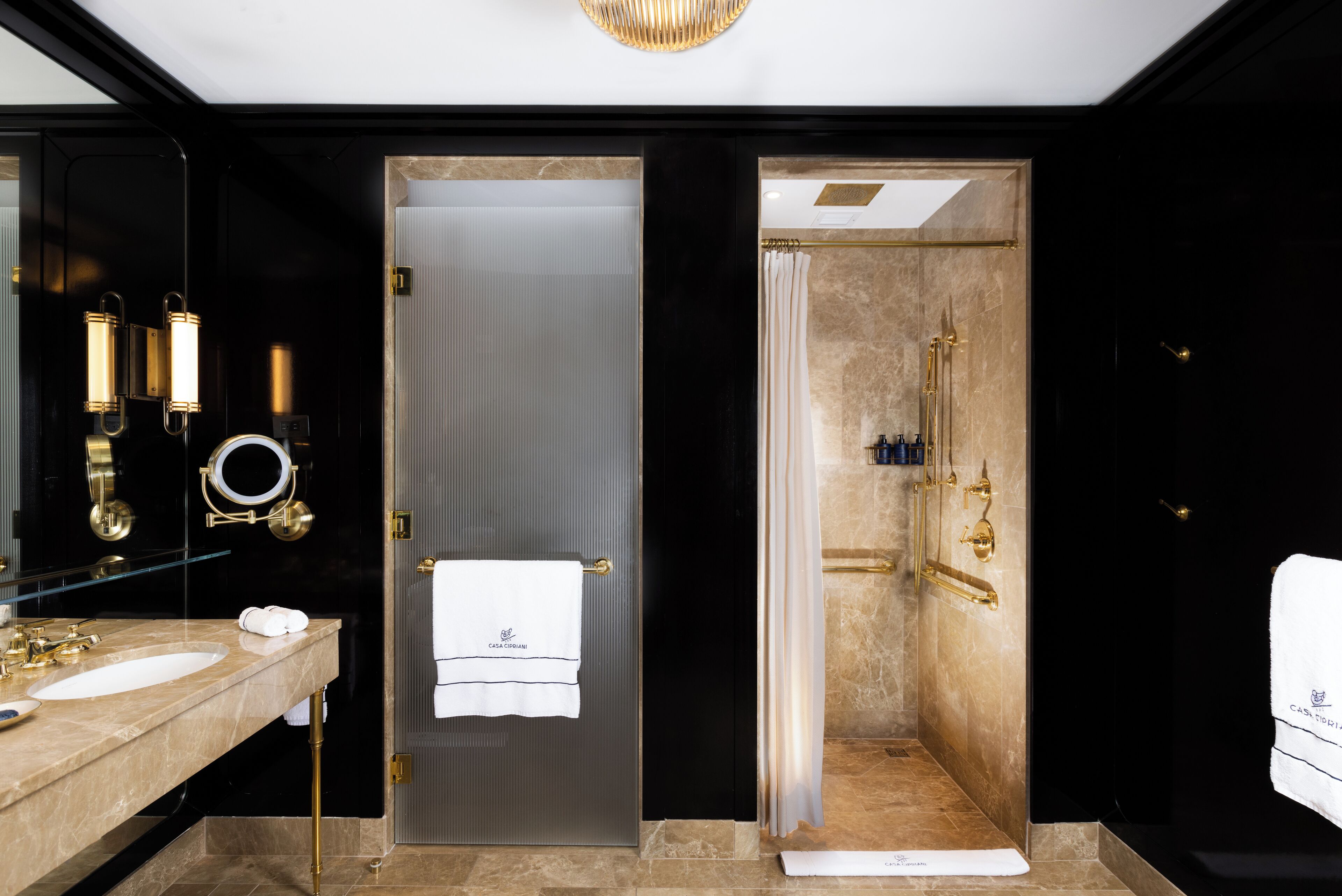 Een moderne badkamer met een marmeren wastafel, een glazen deur en een douche met een gouden douchekop.