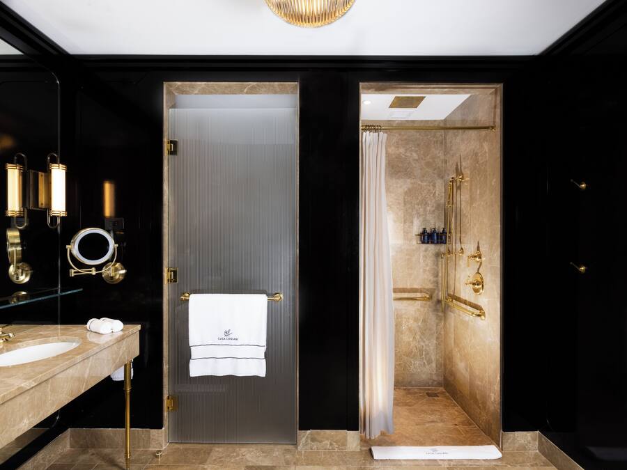 Een moderne badkamer met een marmeren wastafel, een glazen deur en een douche met een gouden douchekop.