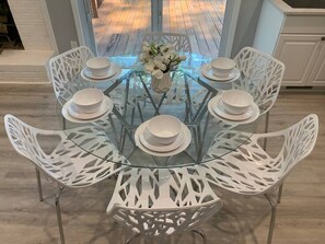 Ett runt glasbord med vita stolar, en vas med blommor och tallrikar och skålar som är framdukade för måltiden.