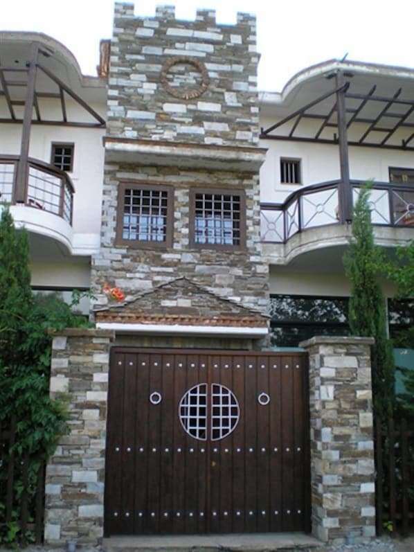 A building with a stone facade, a central tower with a circular window, and a large wooden gate with a grid design. - Kornilia Villa (Agia)