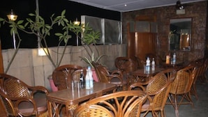 A restaurant with wicker chairs and tables, potted plants, and a stone wall. - Royal Palace (New Delhi)