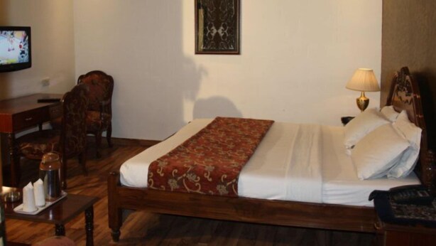 A hotel room with a wooden bed, a desk with a chair, a television, and a lamp. - Royal Palace (New Delhi)