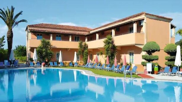 Ein Hotel mit Schwimmbad, Liegestühlen und Palmen.