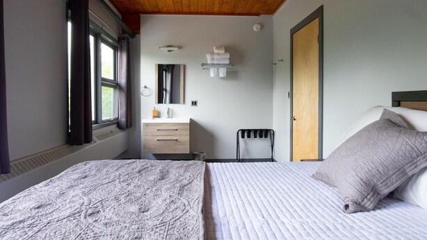 Um quarto com uma cama, uma cadeira, cômoda, espelho e janela.
