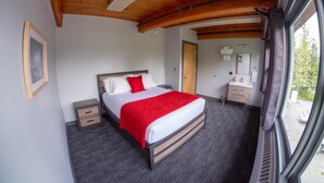 Quarto com cama, mesa de cabeceira, cômoda, janela e porta.