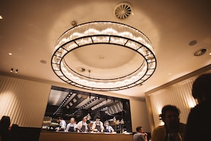 A restaurant interior with a circular chandelier, a bar area, and a group of people. - Beaumont (Maastricht)