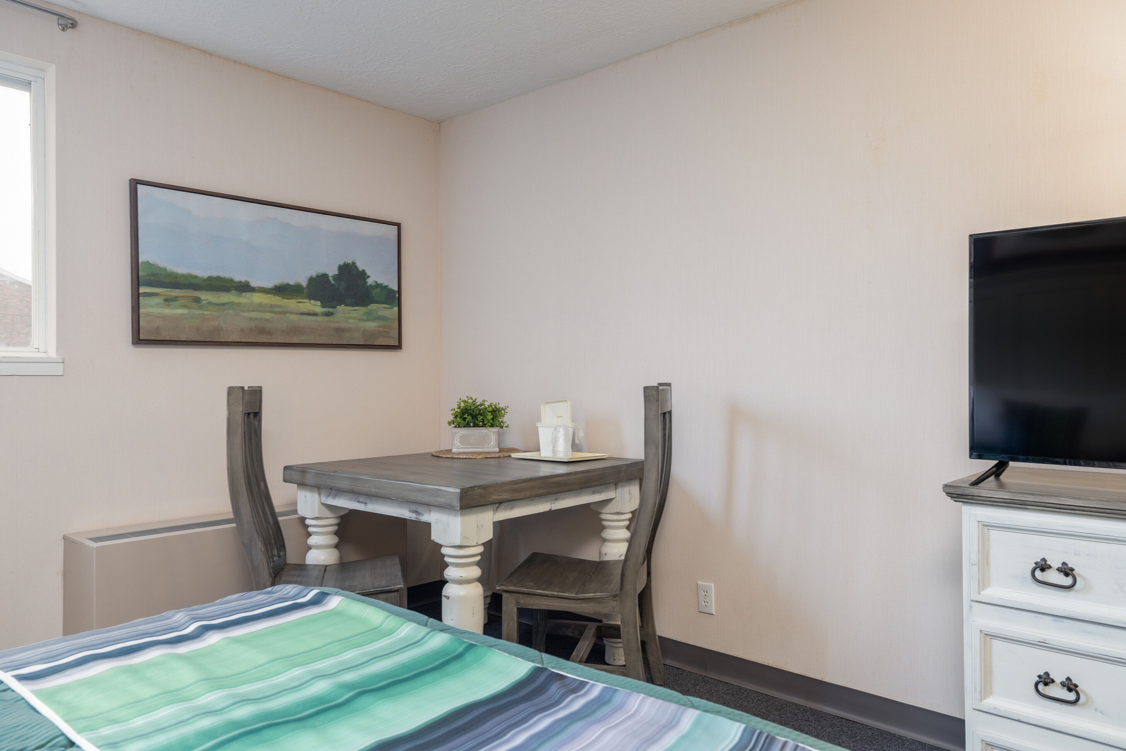 Une chambre à coucher comprenant un lit, un bureau avec une chaise, une télévision et une commode.
