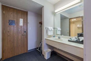 A hotel bathroom with a wooden door, a sink, a mirror, and a trash bin.