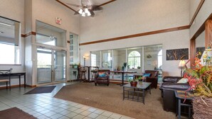 A spacious lobby with a high ceiling, a seating area with leather sofas, a coffee table, and a large mirror reflecting the interior.