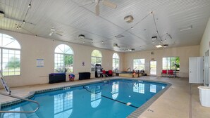 An indoor swimming pool with clear blue water, surrounded by windows and equipped with a ceiling fan and lights.