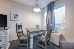 A room with a wooden dining table, two chairs, a television, a potted plant, a window with curtains, and a radiator. - Buffalo Lodge (Buffalo)