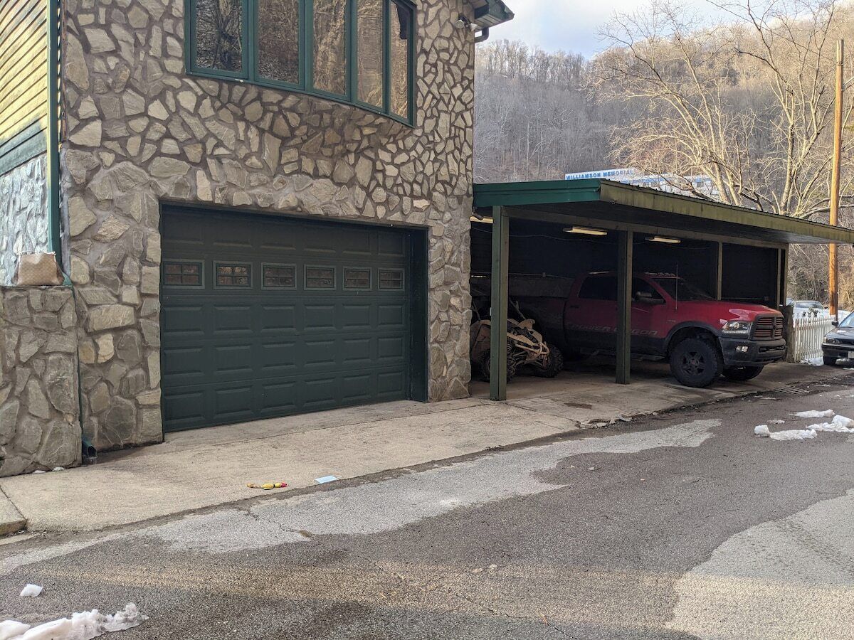 Ein Steinhaus mit Garage und überdachtem Parkplatz.