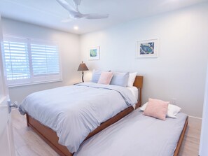 A bedroom with a large bed, a smaller bed, a ceiling fan, and two wall-mounted paintings.