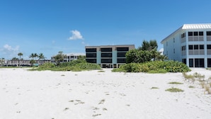 Un hôtel en bord de mer, composé de plusieurs bâtiments à étages, avec une plage de sable en premier plan et des palmiers.