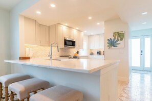 A modern kitchen with a central island, stainless steel appliances, and light-colored cabinetry.