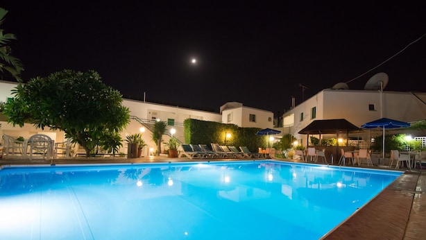 A swimming pool with lounge chairs and umbrellas, surrounded by buildings and greenery. - Eligonia Apartments (Ayia Napa)