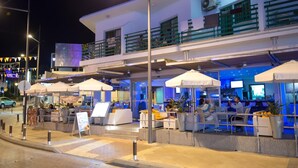 A modern outdoor seating area with umbrellas, a bar, and a poolside lounge. - Eligonia Apartments (Ayia Napa)