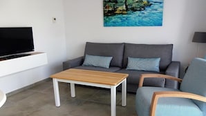 A modern living room with a grey sofa, a wooden coffee table, a TV on a white stand, and a painting of a blue seascape. - Playamar (Tías)