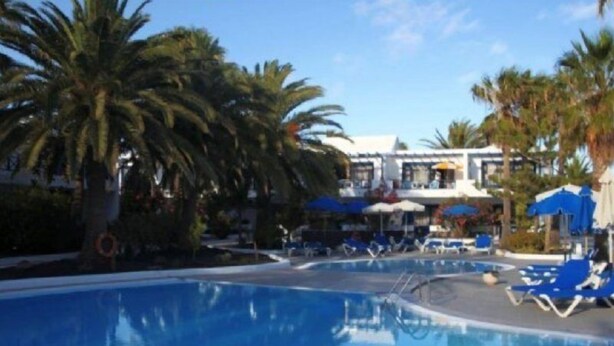 A clear blue pool with lounge chairs and umbrellas, surrounded by palm trees and a building with a white facade. - Playamar (Tías)