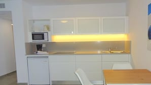 A compact kitchenette with a microwave, sink, and small refrigerator. There is a wooden table and two white chairs. - Playamar (Tías)