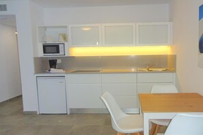 Compact kitchenette with microwave, refrigerator, and sink, featuring a dining area with a table and chairs.