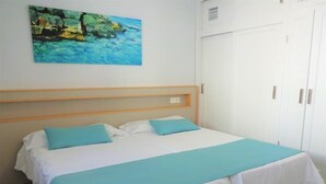 A neatly made bed with a white and teal bedspread, a teal pillow, and a wooden headboard. - Playamar (Tías)