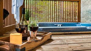 Un tavolo di legno con un vassoio che contiene una bottiglia di Dark Horse Pinot Noir, un bicchiere di vino e una candela. Sullo sfondo, un patio in legno con una vasca idromassaggio blu e vista sul verde.