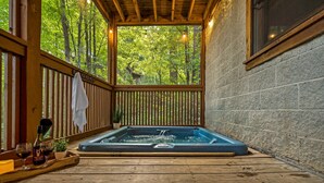 Un patio in legno con vasca idromassaggio, ringhiere in legno e vista su una foresta.