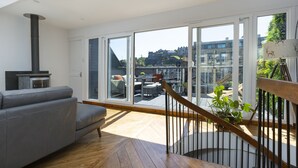 A modern living room with a grey sofa, a wooden floor, and a large window offering a view of a cityscape. - The Edinburgh Rooftop Terrace (Edinburgh)
