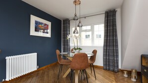 A dining area with a round table, brown chairs, a white radiator, a window with curtains, and a ceiling light fixture. - The Edinburgh Rooftop Terrace (Edinburgh)