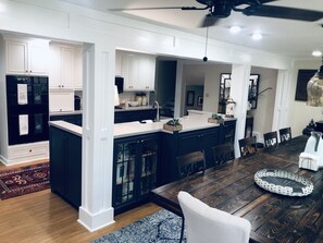 A modern kitchen with dark cabinetry, a central island, and a dining area with a wooden table and chairs. - MASTERS 2021 RENTAL IN AUGUSTA, GA (Augusta)