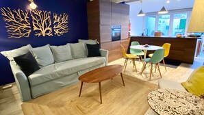 Een moderne woonkamer met een bank, salontafel en stoelen. In de achtergrond is een keuken met een eettafel en stoelen te zien.