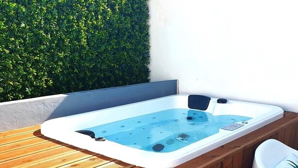 Een hottub met een houten terras en twee witte stoelen met bloemenkussens.